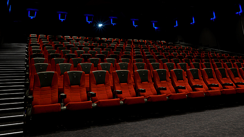 Foran en tom biografsal med mange røde biografstole og blå spotlamper på væggene