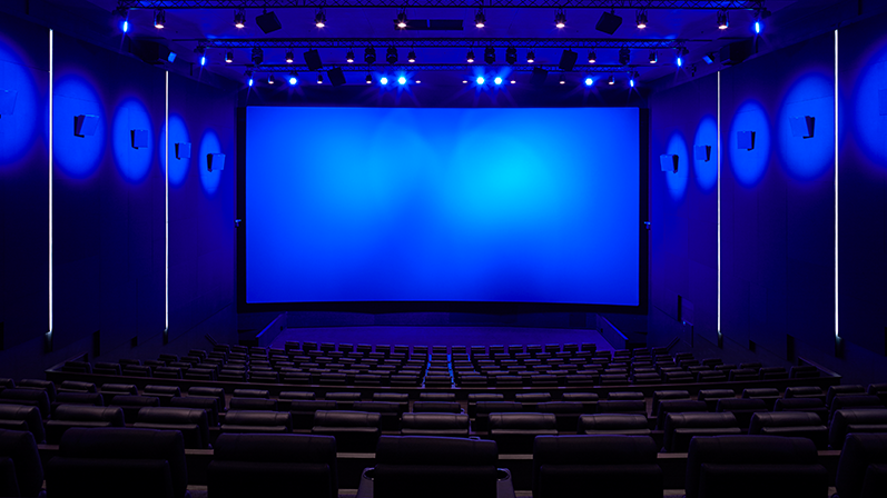 En stor og tom biograf med mange siddepladser og blå belysning på loft, vægge og lærred