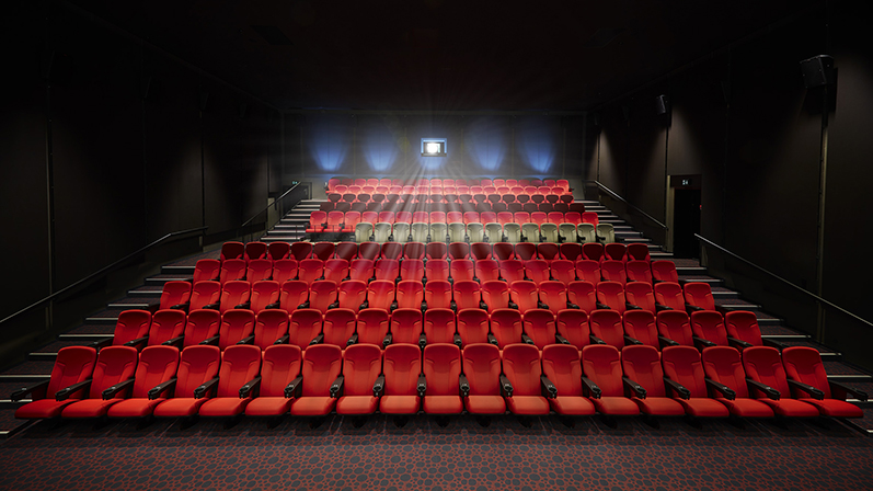 En tom biografsal med mange tomme siddepladser i rød. Væggene er sorte med blå spotlys