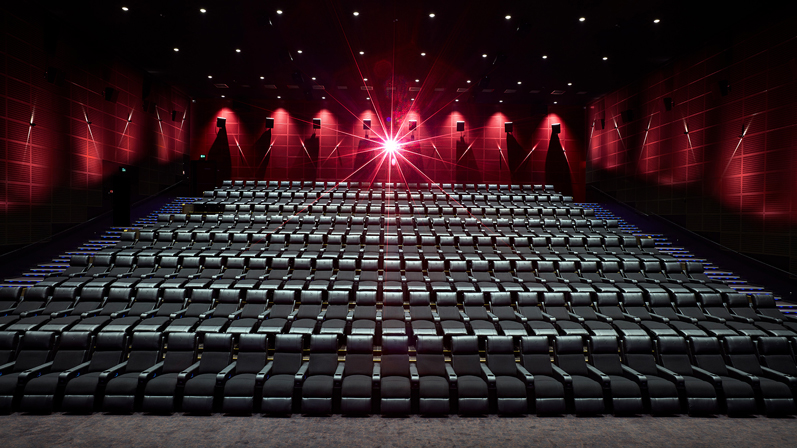 En moderne biograf med store biografsæder i sort læder. Væglamperne er røde og der er en skarp projektor