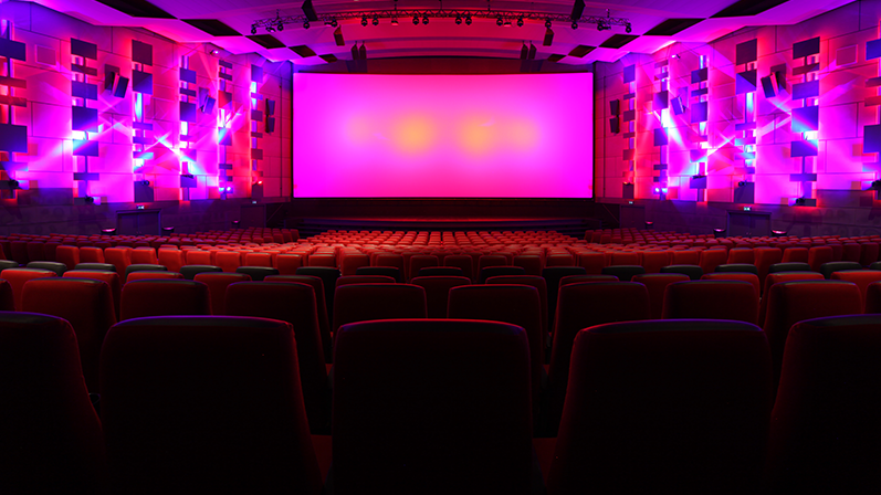 En tom biografsal med mange tomme biogradsæder og et stort biograflærred belyst med lyserøde lamper