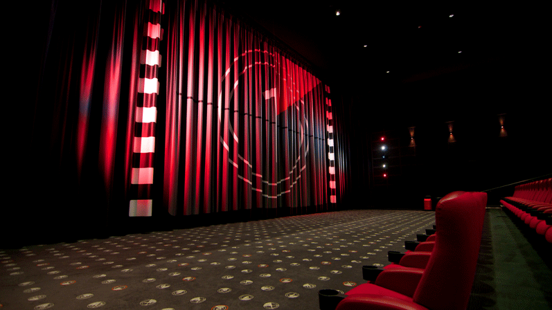Et stort biograflærred med nedtælling i midten. I rummet er der røde gardiner og mange toppe siddepladser